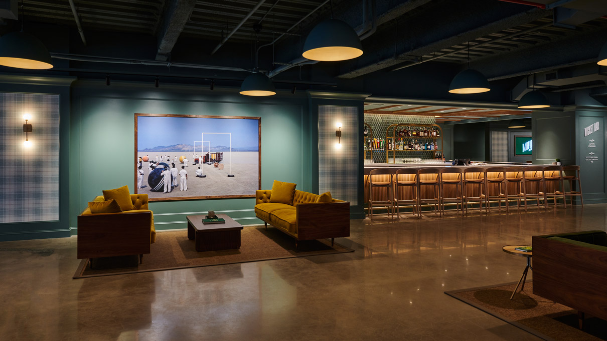 A cozy lounge area with yellow armchairs, a coffee table, and a bar in the background, with subdued lighting creating a warm ambiance.