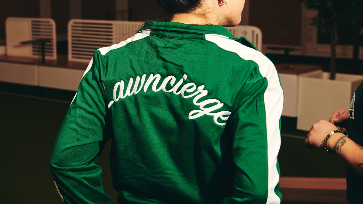 A person is seen from behind, wearing a green jacket with the word ”lawncierge
